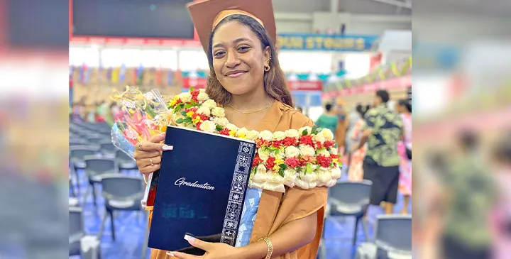 A photograph of graduate Jessie Mule Siga holding her graduation certificate while dressed in graduation attire on April 10, 2025.