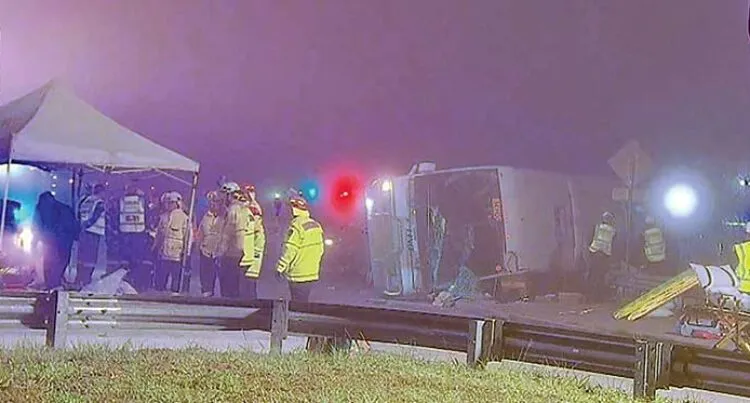A photograph of a bus on it's side, surrounded by first responders.