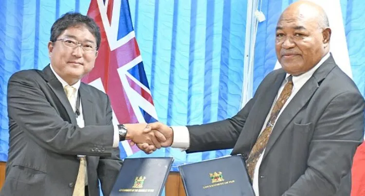 A photograph of Japan International Cooperation Agency Resident Representative Satoshi Wakasugi (left) shaking hands with Ministry of Policing permanent secretary Berenado Daveta following the agreement on June 24, 2025.