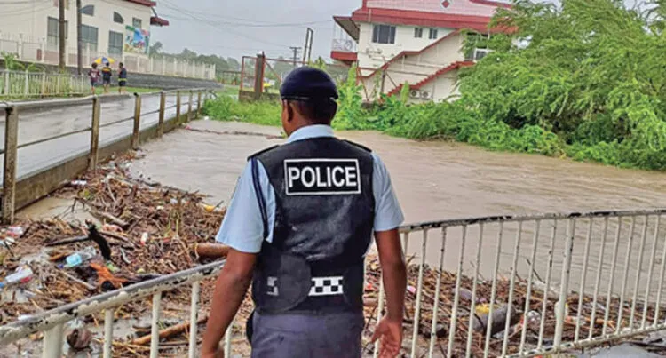 A police officer looks at a burst river bank from behind a fence.